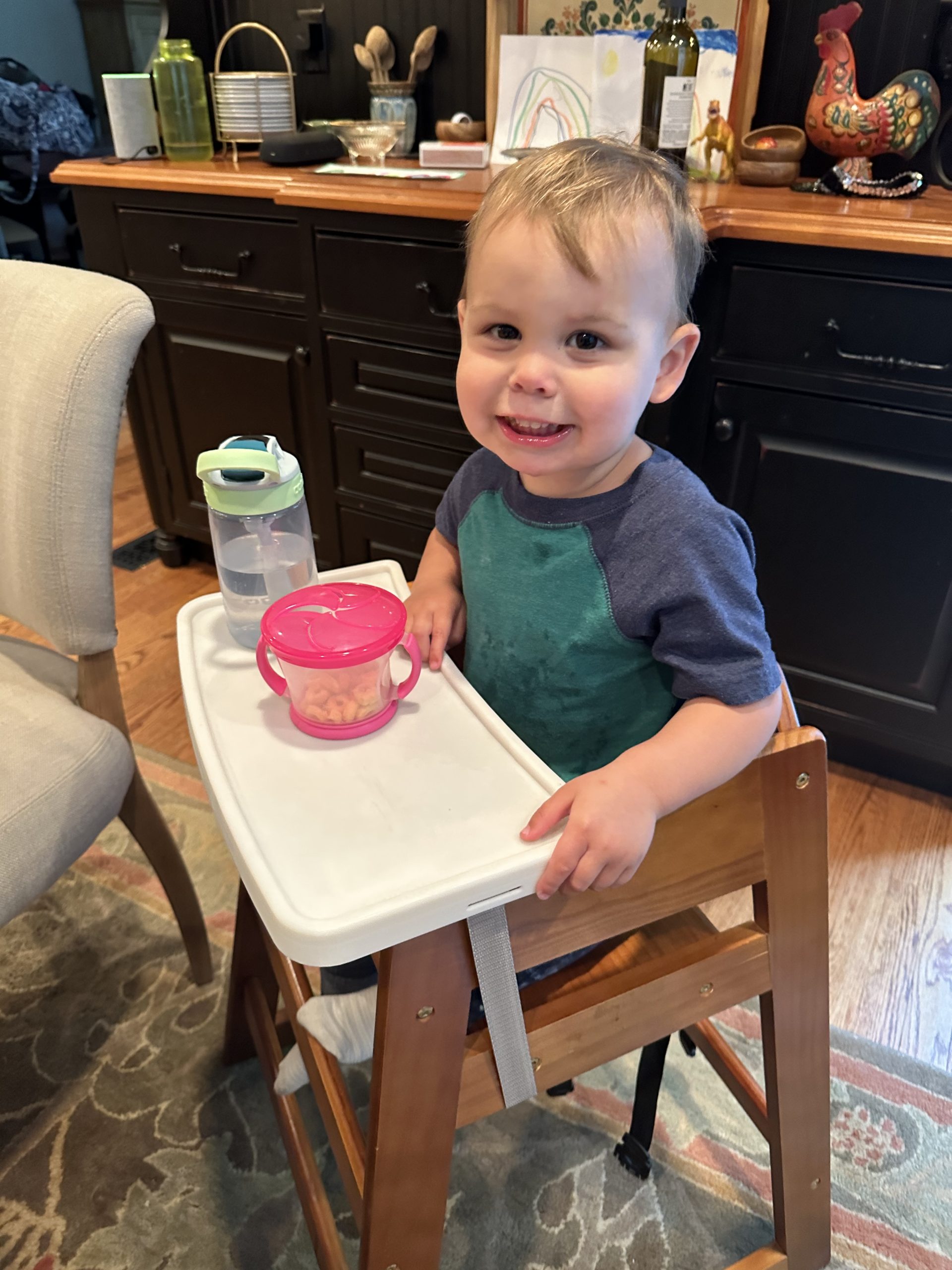 Happy young boy eating with "dine out tray" on wooden high chair.